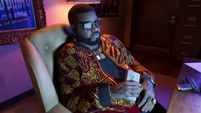 Boobie Ike counts cash in an office chair, a pistol on the desk